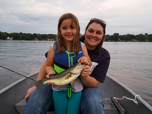 Young girl holding bass she caught with mother in background
